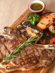 Grilled beef steak with rosemary on a wooden board, served with roasted zucchini and peppers.