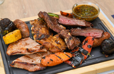 Grilled meat with vegetables and sauce on a wooden board, close-up