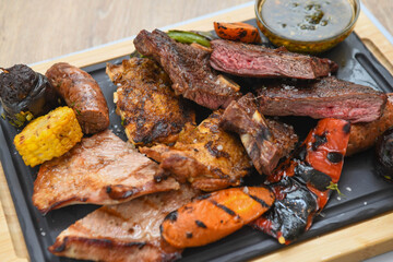 Grilled meat with vegetables and sauce on a wooden board, close-up