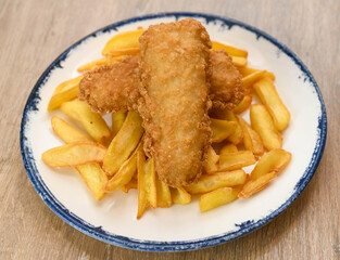 Fried fish fingers with french fries on a plate, close up