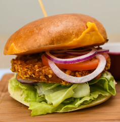 Chicken burger with lettuce, onion, cheddar cheese and tomato on a wooden board.