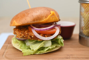 Chicken burger with lettuce, onion, cheddar cheese and tomato on a wooden board.