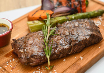 Beef steak with rosemary and vegetables on a wooden board.