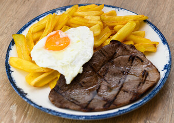 Grilled beef steak with fried egg and french fries on a plate