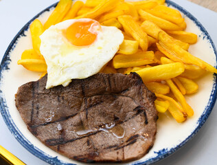 Grilled beef steak with fried egg and french fries on a plate