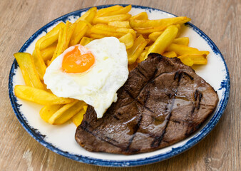 Grilled beef steak with fried egg and french fries on a plate