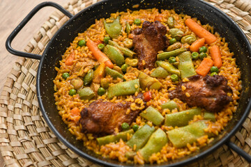 Paella with meat, rice and vegetables in a wicker plate