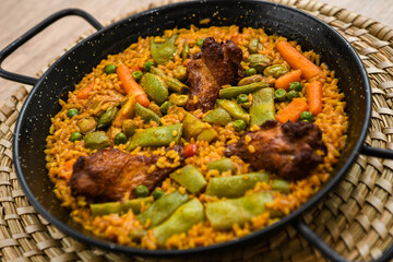 Paella with meat, rice and vegetables in a wicker plate
