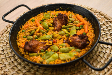 Paella with meat, rice and vegetables in a wicker plate