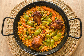 Paella with meat, rice and vegetables in a wicker plate