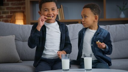Two little African American boys drinking milk with tasty cookies Kids sons hungry children drink eating breakfast at home happy cute pretty adorable siblings health care healthy food nutrition eat