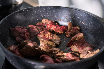 Sliced liver sizzles in a pan with chopped onions, releasing savory aromas