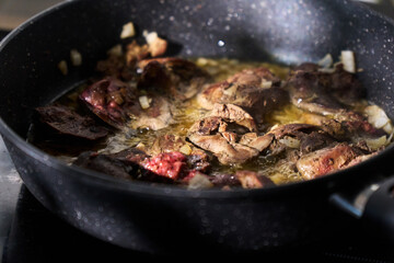 Cooking liver pieces in a frying pan with steam rising and kitchen appliances in the background