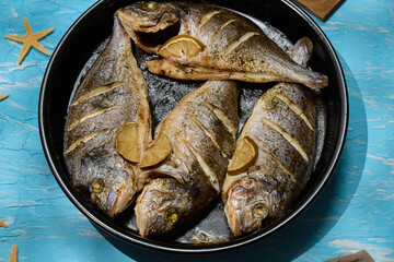 Freshly cooked dorado with lemon slices served on a rustic table with sea stars and coarse salt
