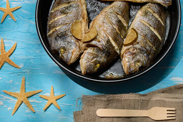 Freshly cooked dorado with lemon slices served on a rustic table with sea stars and coarse salt