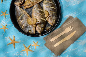 Fresh dorado fish arranged on a serving plate with lemon slices and sea salt on a bright blue background