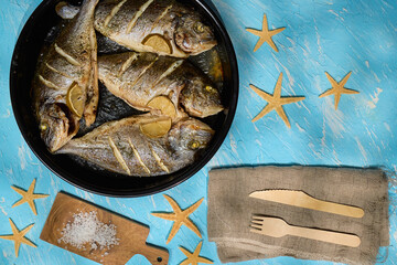 Fresh dorado fish arranged on a serving plate with lemon slices and sea salt on a bright blue background