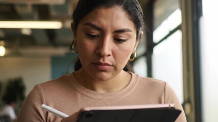 Concentrated Hispanic woman working on digital tablet with stylus indoors, using technology. - Powered by Adobe