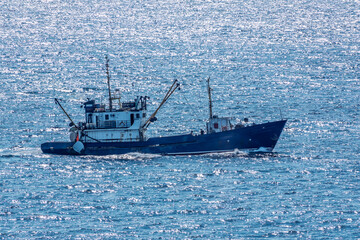 Fishing boat in blue sea and clear sky with birds flying overhead.