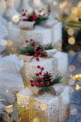 Festive holiday scene featuring beautifully wrapped Christmas presents with pinecone and red berry decorations, set under white Christmas tree adorned with glowing lights.