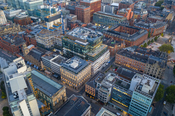 Aerial view of central Manchester in early daylight showing modern offices, cranes, and historic red-brick buildings.
