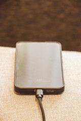 A smartphone connected to a charging cable lying on a soft fabric surface. The device appears sleek and modern, emphasizing the importance of technology in daily life.