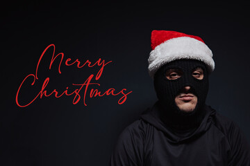 Masked robber and Christmas hat on a black background and Merry Christmas text