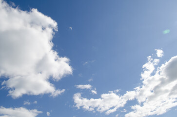 A clear blue sky with fluffy white clouds scattered throughout. The scene conveys a sense of tranquility and openness, ideal for nature themes.
