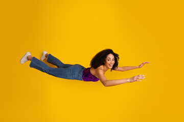 Young woman in jeans and purple top flies through a yellow background capturing energy and carefree...