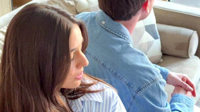 Serious couple sitting on sofa at home talking and confronting each other, thoughtful and sad mood as if during relationship therapy or difficult conversation, concept of communication, crisis and emo