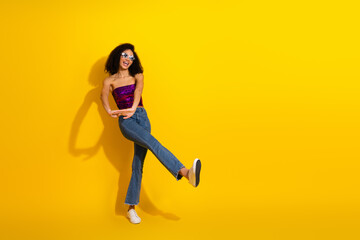 Young stylish woman dancing in a vibrant yellow studio wearing a glitter top and jeans for fashion lifestyle and festive party vibe