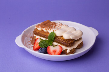 Tiramisu with berries and mint - classic dessert in white bowl on purple