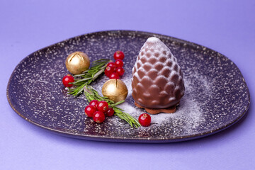 a dessert in the shape of a chocolate pine cone, decorated with berries on a purple background