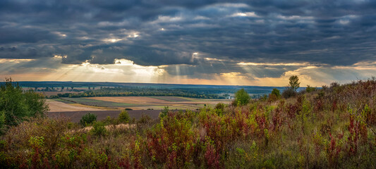 Autumn nature landscape with forests, fields on the horizon under a stormy sky with sun rays