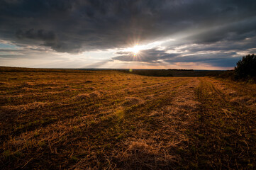 The sun breaks through the clouds, field with golden light after the harvest