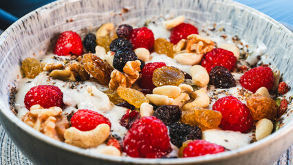 A vibrant and healthy yogurt bowl topped with fresh raspberries, a mix of nuts and dried fruits, chia and pumpkin seeds. A delicious and nutritious breakfast or snack.