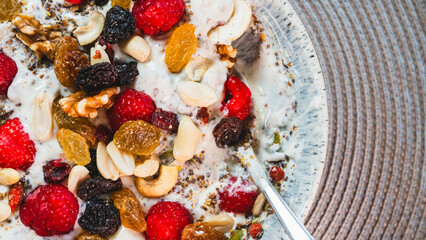 A vibrant and healthy yogurt bowl topped with fresh raspberries, a mix of nuts and dried fruits, chia and pumpkin seeds. A delicious and nutritious breakfast or snack.
