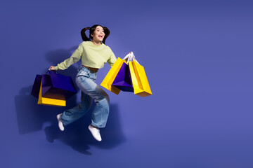 Happy young woman jumping with shopping bags against a vibrant purple background promoting casual...