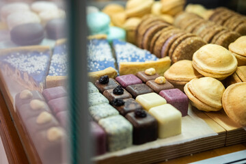 A variety of biscuits, cookies, and petit fours are neatly displayed in a glass bakery showcase....