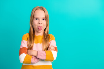 Expressive young girl in striped sweater on teal background making playful gesture with hands folded and tongue out © deagreez