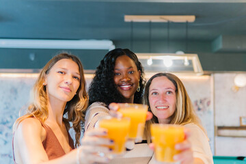 Diverse women friends celebrating friendship, enjoying orange juice in vibrant glasses, smiling and cheering for a happy moment together