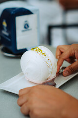 Pistachio macaron indulgence. Close-up reveals a silver spoon poised over the delicate confection on a white plate, with a coffee cup nearby. Soft light accentuates pink and green tones.