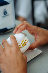 Sweet pistachio macaron close-up. Delicate hands hold the treat, revealing vibrant green nuts in creamy meringue. Minimalist presentation on a clean white plate. A moment of indulgence.