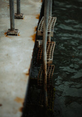 Dark canal steps metal texture. Venice Italy. Rusty ladder reflection water surface. Aged industrial aesthetic. Gritty urban decay background. Atmospheric moody scene.
