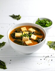 White bowl of miso soup with tofu, seaweed, and sesame