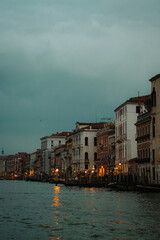 A picturesque view along a Venetian canal as dusk settles. Warm lights glow from the historic buildings, reflecting beautifully on the water's surface creating a magical and tranquil atmosphere.