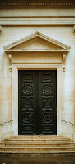 A symmetrical view of a grand, historic stone building featuring elegant wooden double doors. The architectural detail suggests tradition and stability; representing heritage and timeless design.