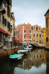 A picturesque view of a Venetian canal, showcasing colorful buildings reflected in the water. Several gondolas are moored along the canal's edge, creating a classic Italian scene.