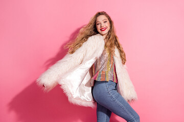 Young woman in a fashionable fur coat posing cheerfully against a vibrant pink background to showcase an elegant lifestyle