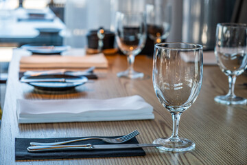 Elegant dining table setting with glassware, cutlery, and napkins arranged neatly on wooden surface, creating a sophisticated atmosphere for a culinary experience